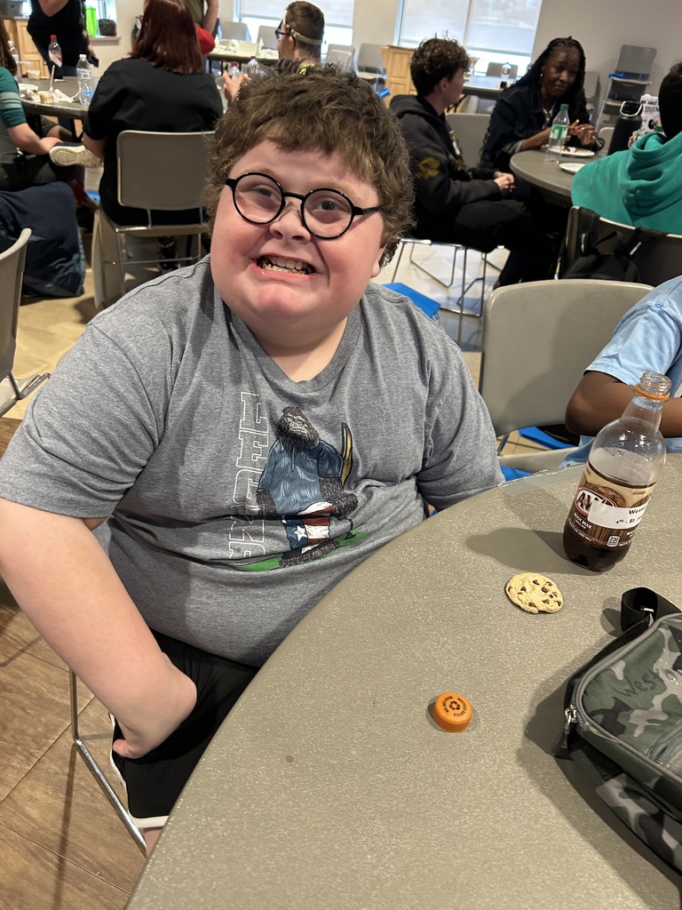 A person in a gray t-shirt sits at a table with a beverage bottle and cookies.