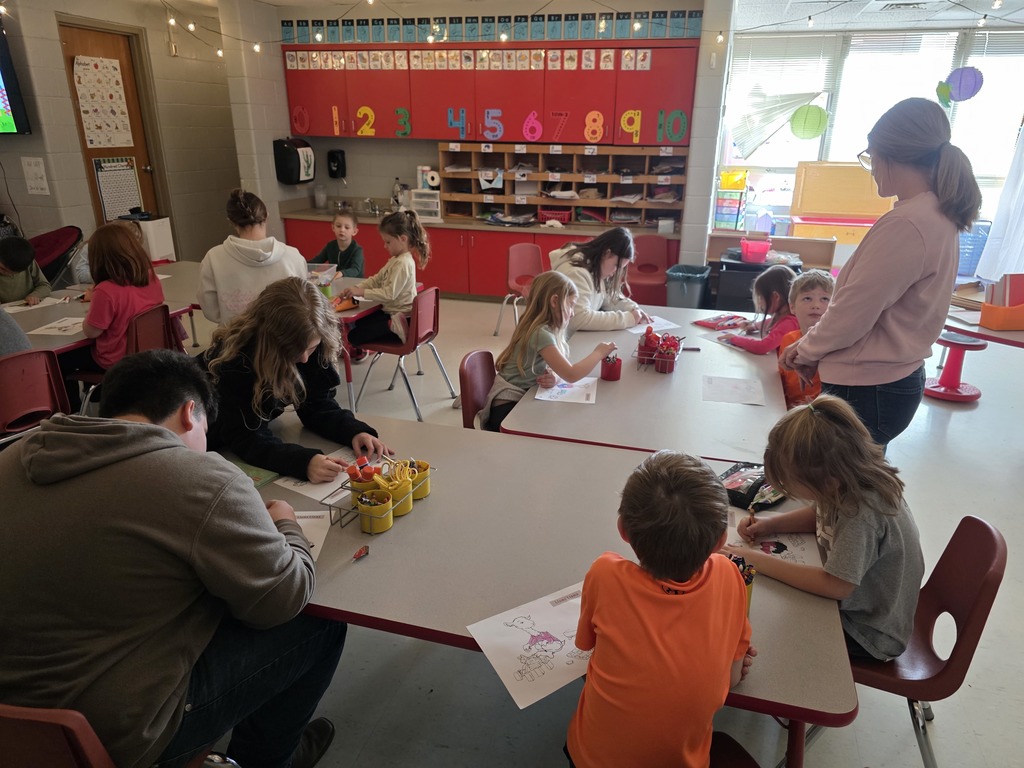 Kids and adults are seated at tables. They are working on art projects. The tables are white.