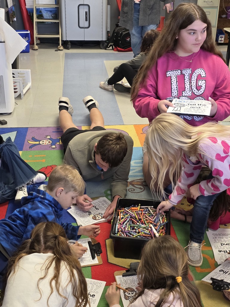 Children seated on a colorful carpet, engaging in coloring activities with a box of crayons and a table with papers.