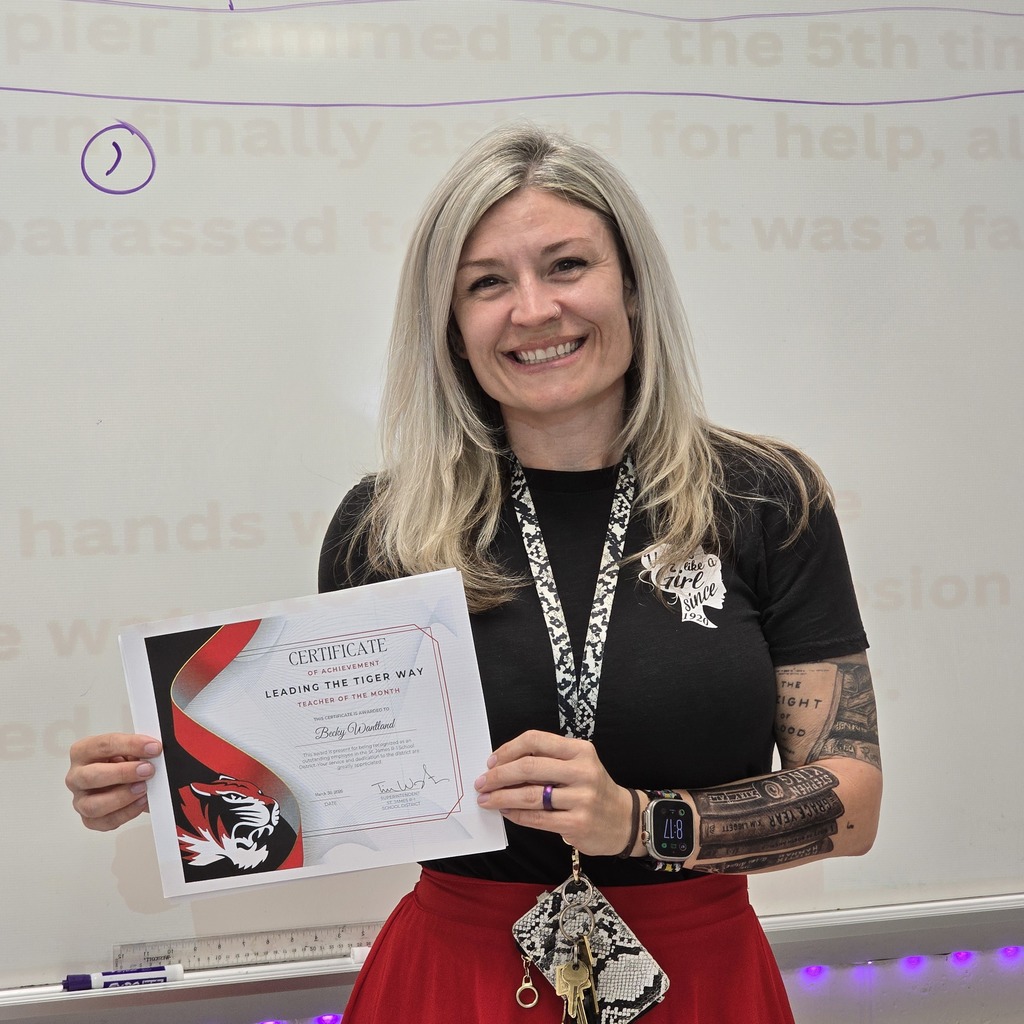 Woman holding certificate in front of whiteboard, wearing black shirt, red skirt, and watch.