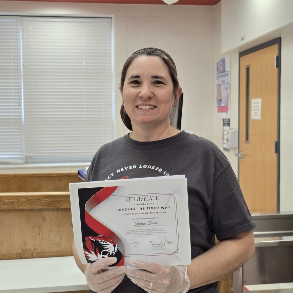 A person wearing a black shirt and gloves holds a certificate. The background shows a door, a window, and a sink.