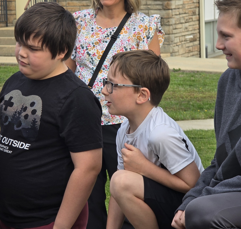 Four children stand on a grassy lawn, one wearing glasses, another with a video game T-shirt.