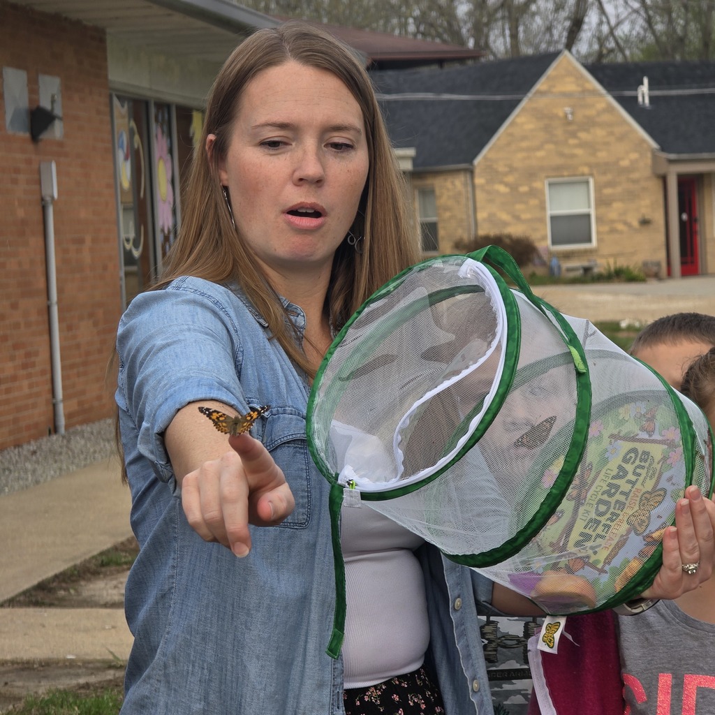 A woman shows a butterfly to a child with a butterfly net in front of a house.