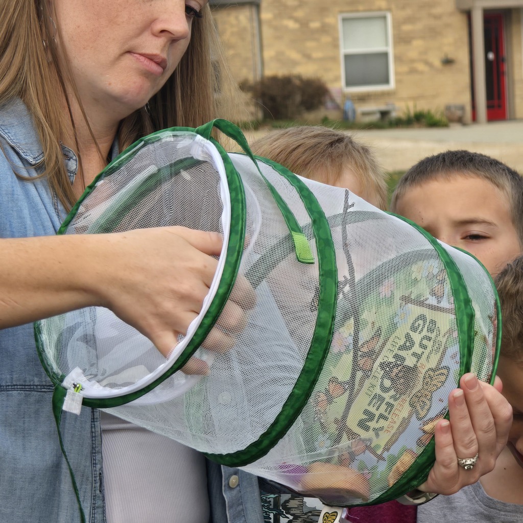 A woman holds a net with a butterfly design in front of a house. A child watches.