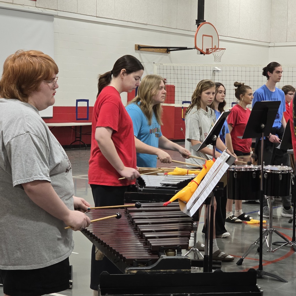 A group of people wearing shirts in various colors, playing drums and xylophones in a gym.