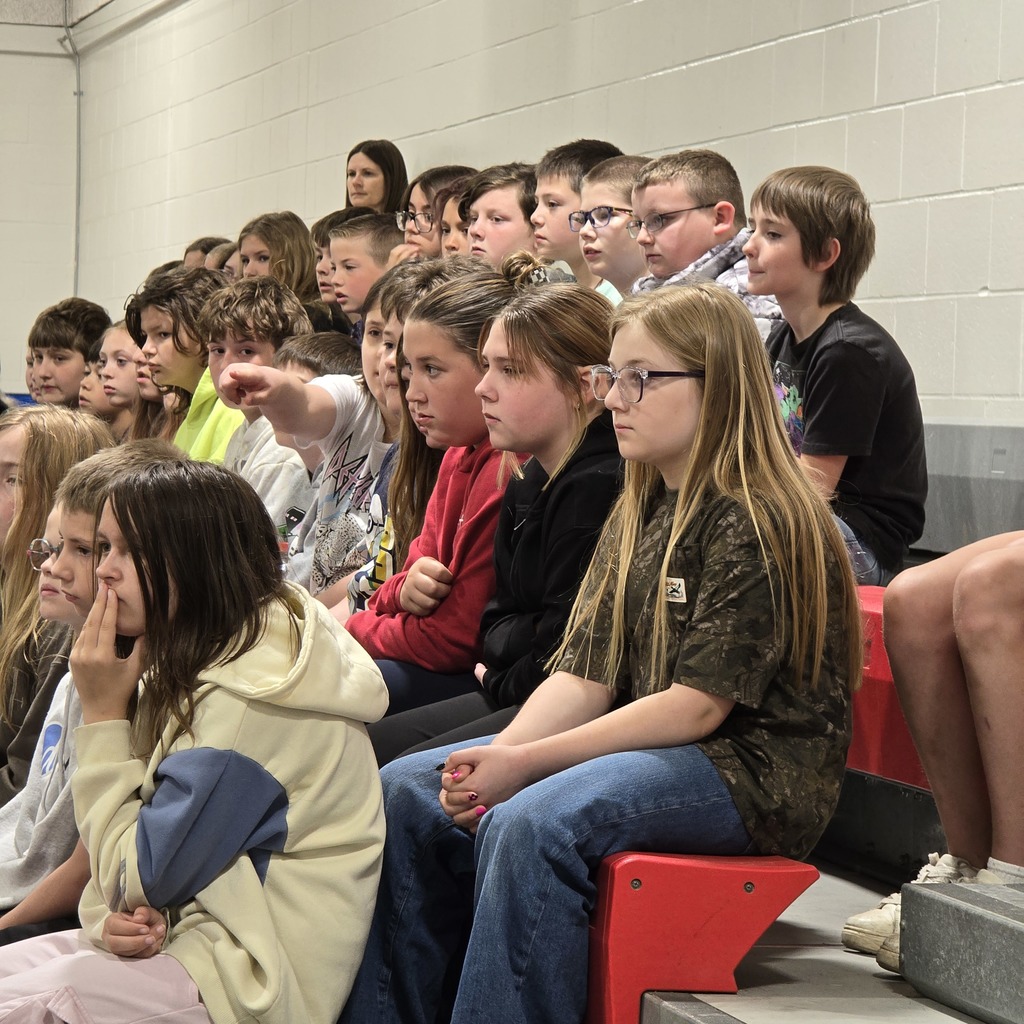 A group of students sits on bleachers; some look engaged while others seem distracted.