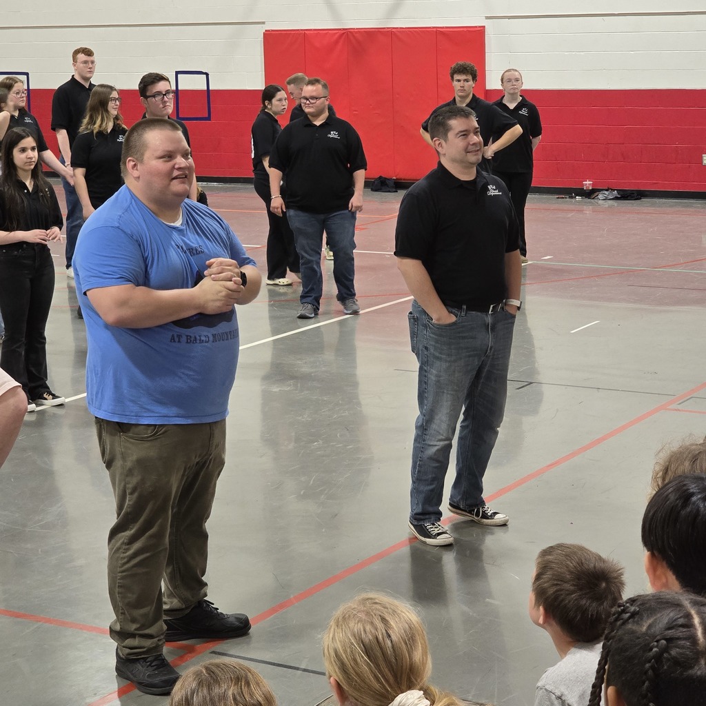 A group of people inside a gym with red walls. Two men stand front and center, while others stand at the back.