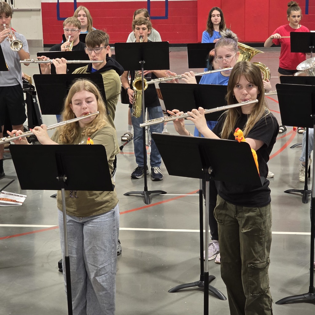 A group of students plays musical instruments in a gym. A girl plays a flute.