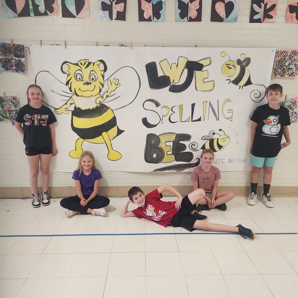 Five children are smiling in front of a colorful banner with the words "LWJE Spelling Bee"