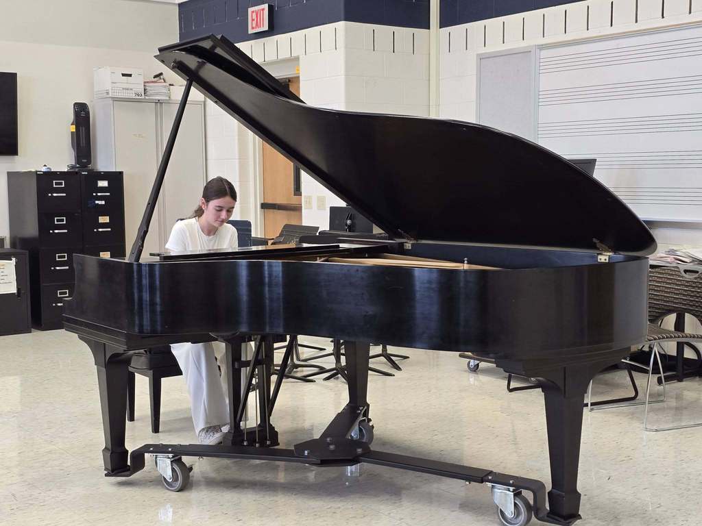 Person sitting at a black grand piano with an open cover in a music room.