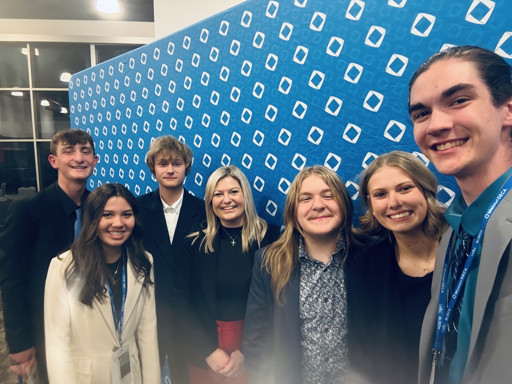 Group of young people smiling and standing next to each other in front of a blue wall.