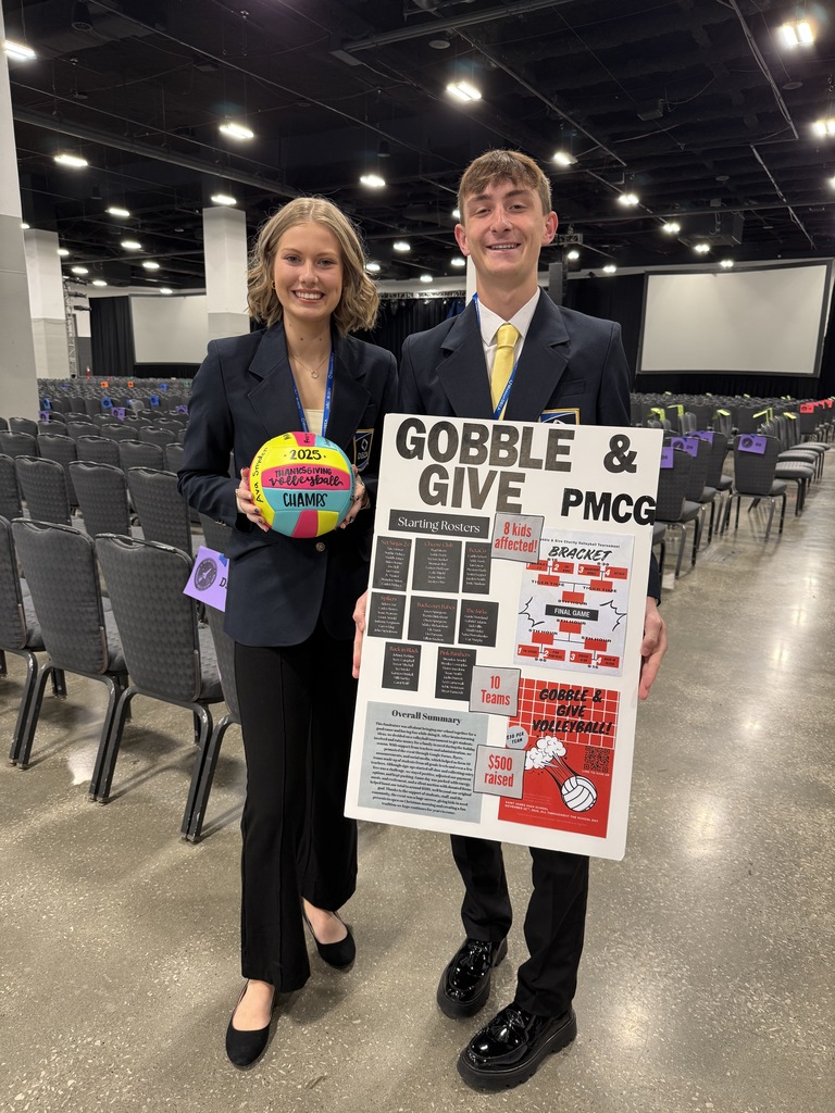 Two people in suits, one holding a colorful ball and a poster, stand next to each other in a conference room.