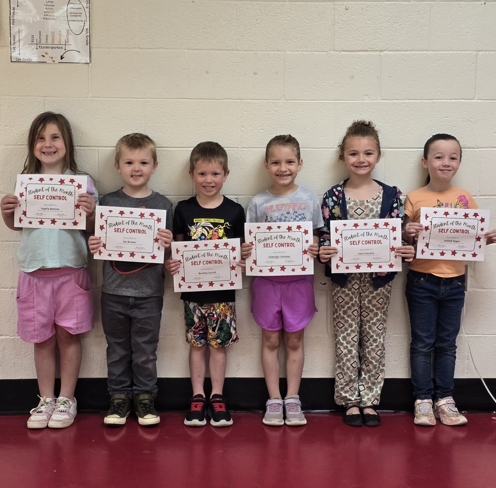 Six children in a school corridor with certificates, standing in a line, and smiling.