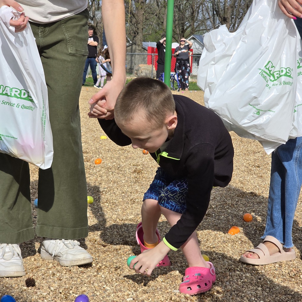 A boy in a black shirt and blue shorts playing with colorful balls on the ground.