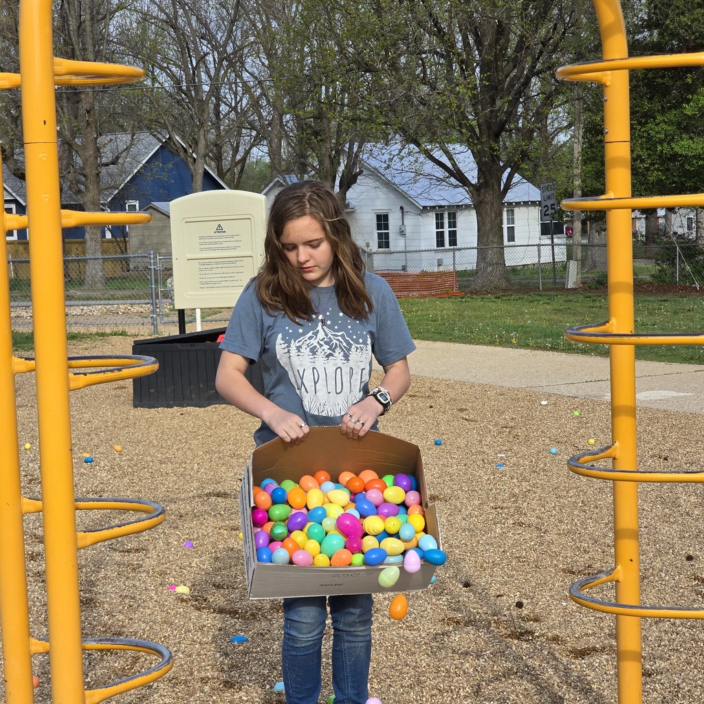 Girl holding a box of colorful eggs in a playground with yellow structures and houses in the background.
