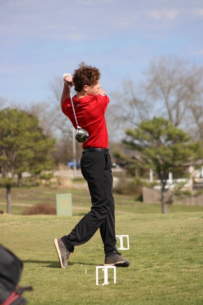 Boy in red shirt swings golf club.