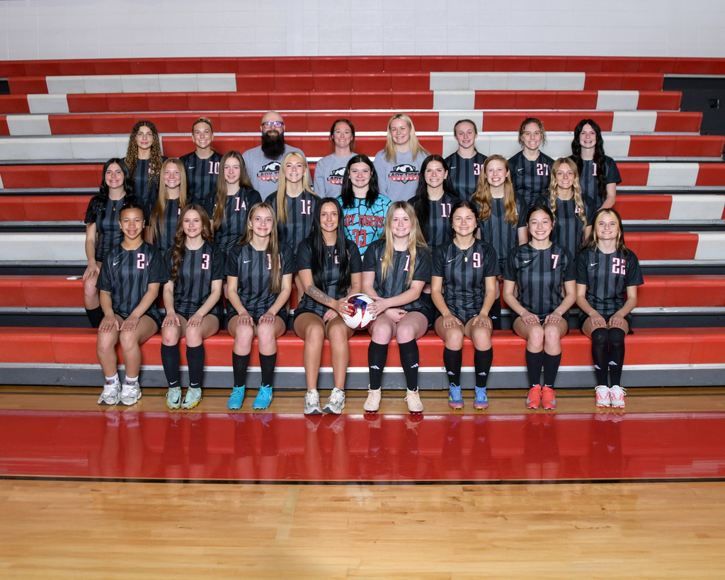 A sports team in matching uniforms, seated and standing on a red bleachers with white stripes.