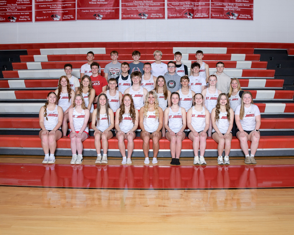 A group of students wearing white shirts and shorts poses for a photo in an indoor sports venue.
