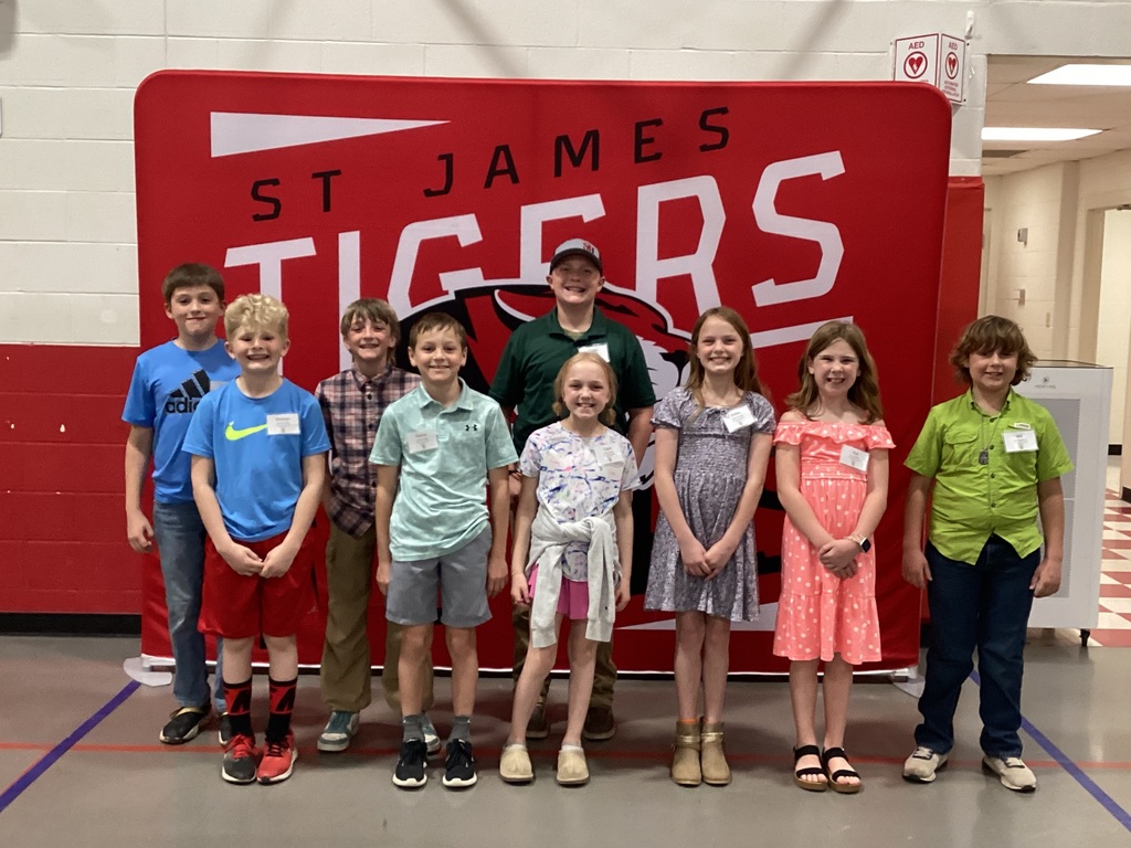 A group of kids and an adult pose in front of a red banner with "St. James Tigers" in white.