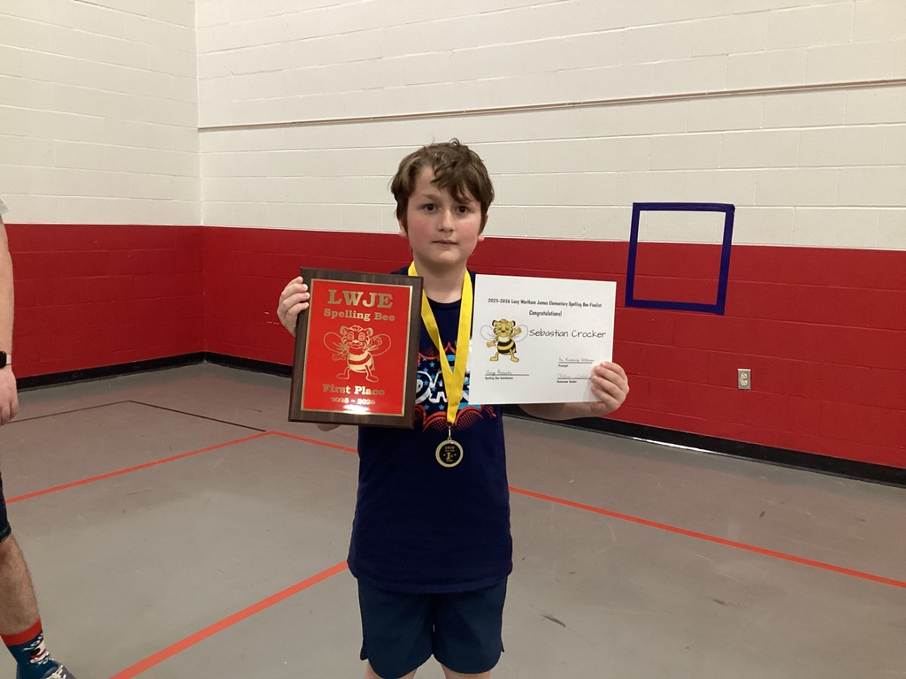 A child holding a certificate and medal inside a gym with red and white walls.