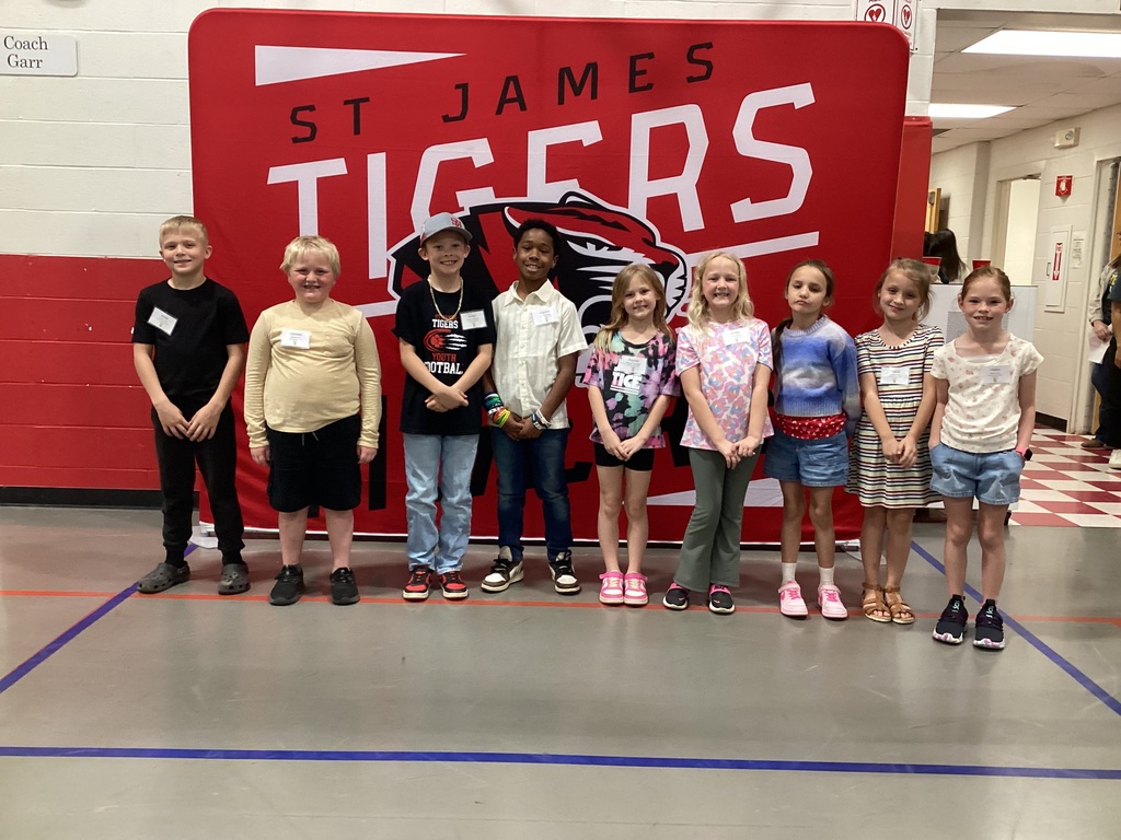 Several children standing in front of a red sign that says "St. James Tigers" in a hallway.