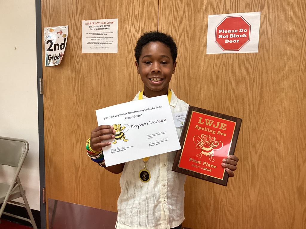 A child poses with a certificate and plaque against a wood-paneled wall with posted signs.