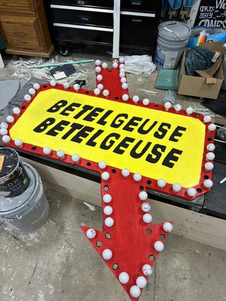 Arrow sign with the words "Betelgeuse Betelgeuse" on it, placed in a room with various items.