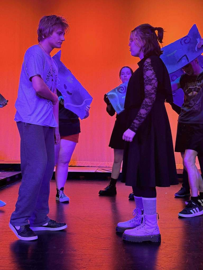 A group of people on a stage with an orange backdrop, wearing casual clothing, holding various items.