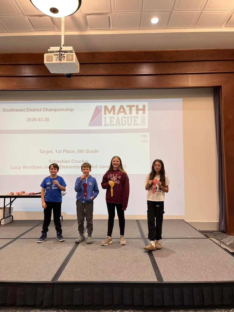 Four children on stage wearing medals. A presentation screen behind them has text reading "MATH LEAGUE".
