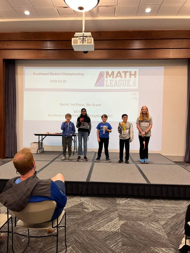 A group of young students stand on stage under a large screen with Math League logo and text.
