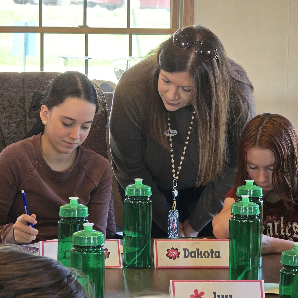 Four people sit around a table with several green water bottles. A woman writes on paper.