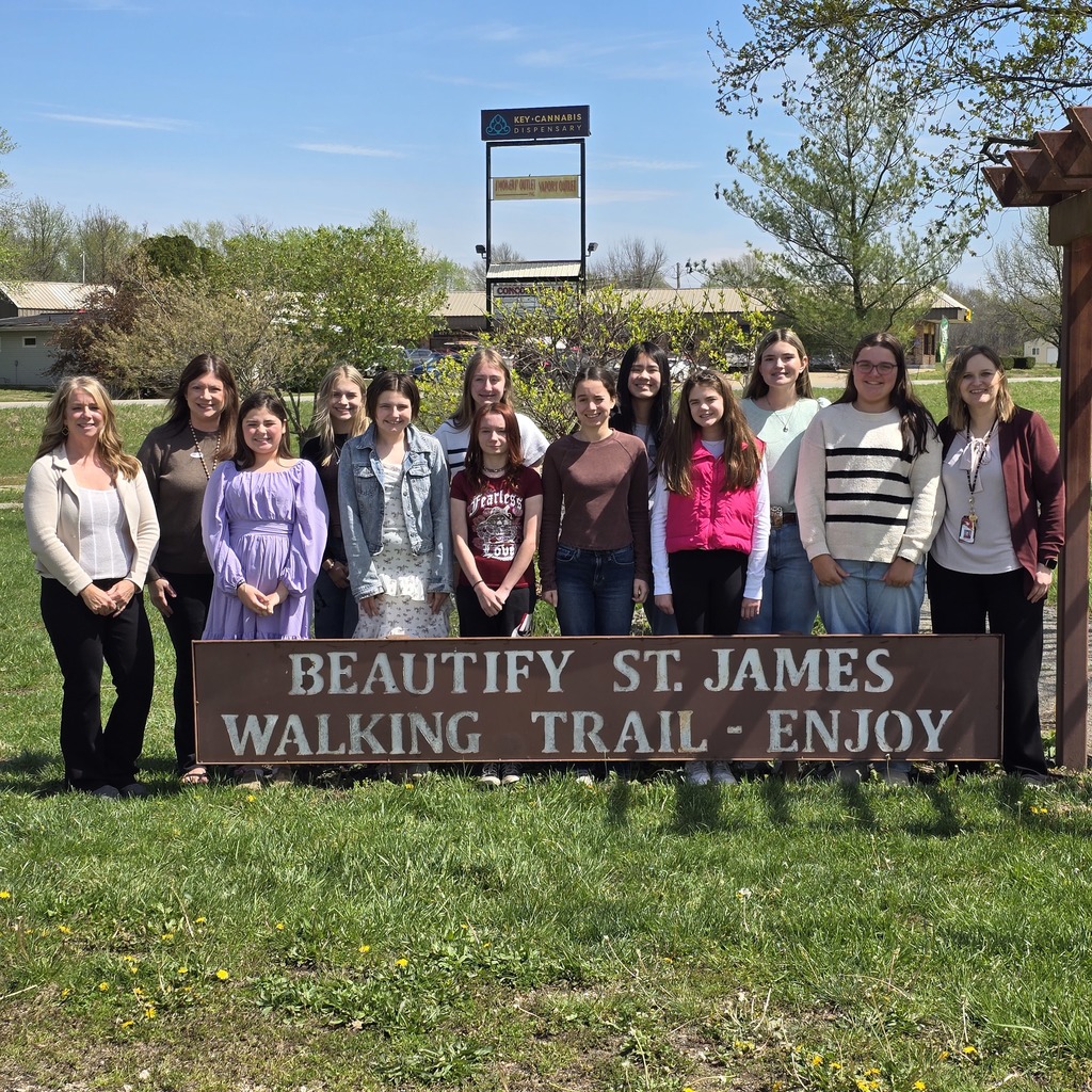 Group of people in various attires, standing together in front of a sign for Beautify St. James Walking Trail.