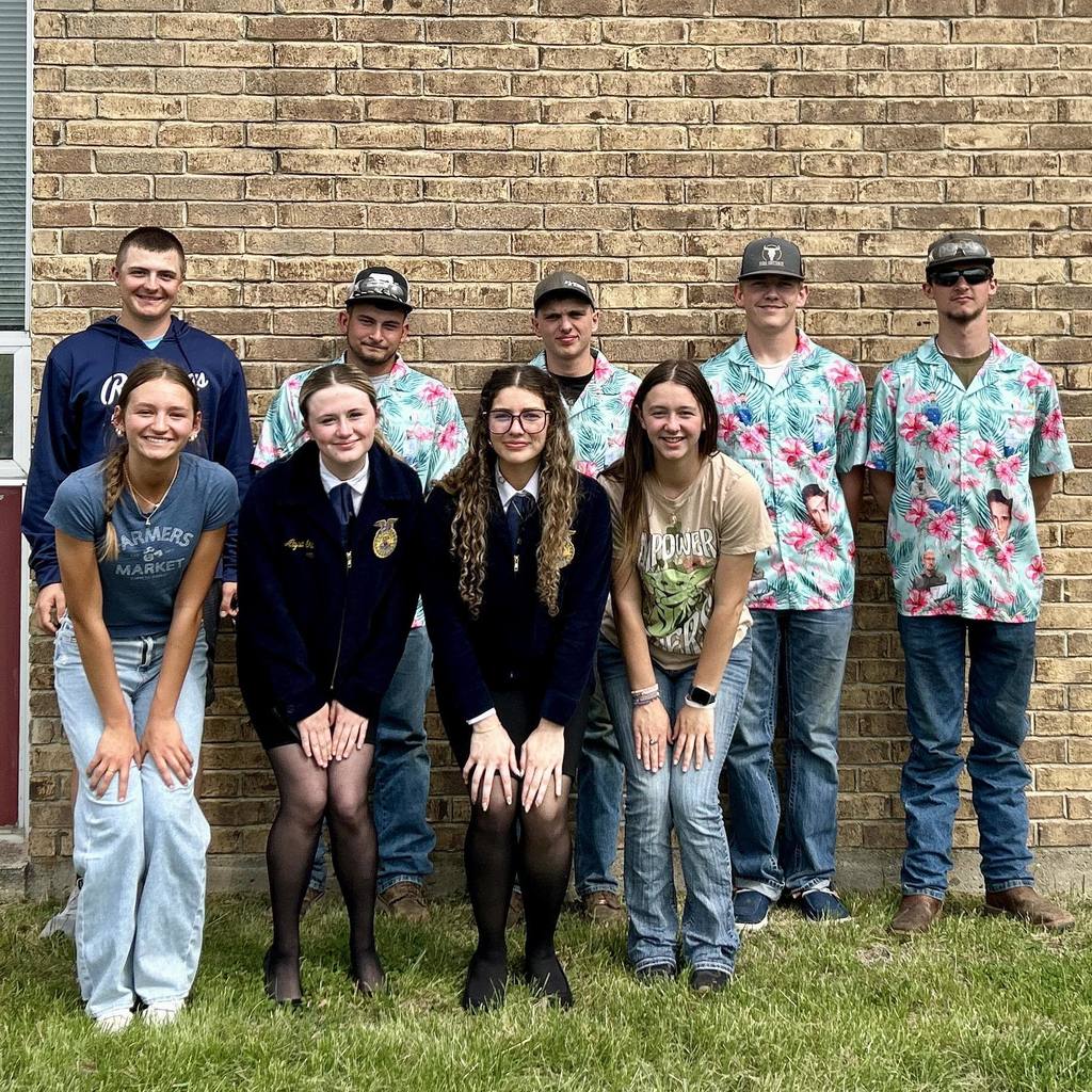 Group of individuals in front of a brick wall. Some wear hats and glasses, others uniforms. Some wear jeans and shirts.