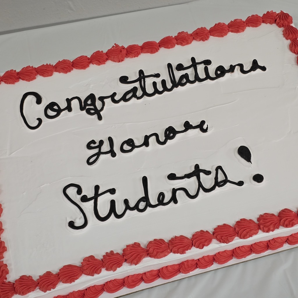 A white cake with a red border features black text reading "Congratulations Honor Students!" The border is decorated with red swirls.