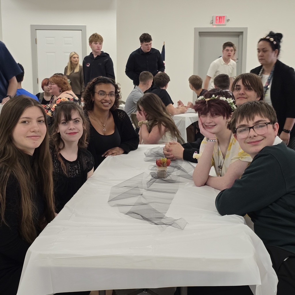 Several people sit at a table, smiling and posing for a photo in a room with white walls.