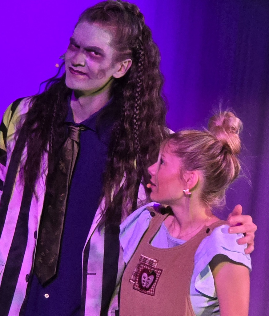 A person in a striped shirt and tie with face paint stands next to a woman with her hair in a bun.