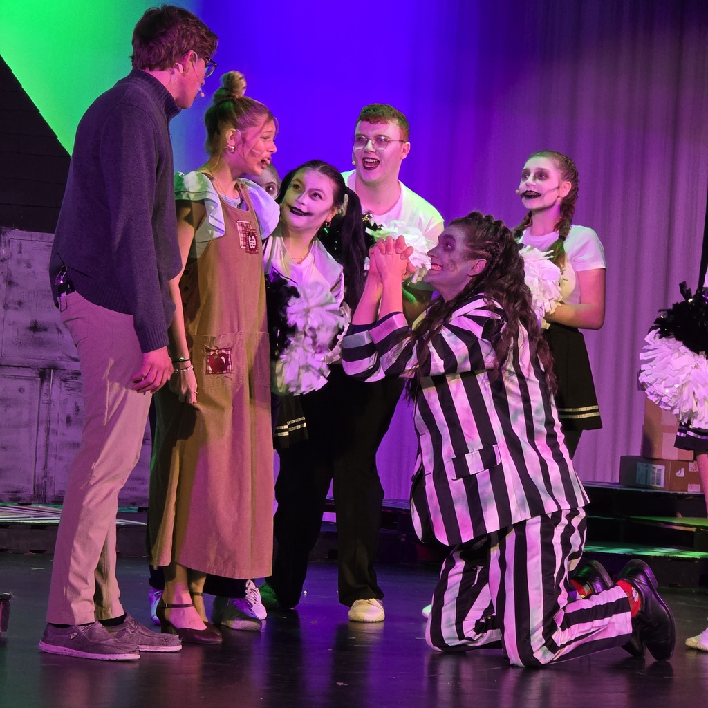 A group of people, including one kneeling, on a stage with purple and green lighting.