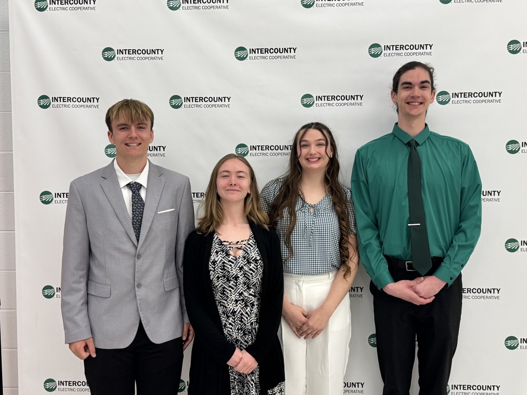 Four individuals in formal attire stand close together. A man and woman on the left wear gray and black. Another woman in white and a man in green are on the right.