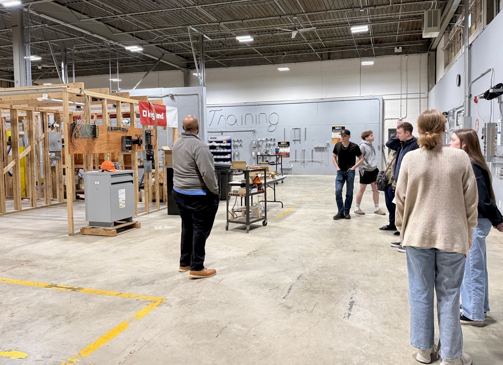 A group of people in a warehouse with construction materials and unfinished walls. Some people are standing while others are walking.