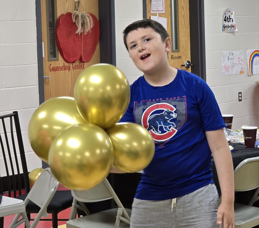 A boy holds gold balloons in a room with doors and tables, a chair, and a black tablecloth.