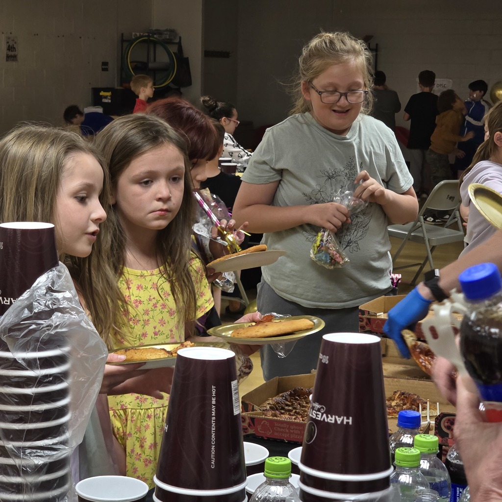 Group of young girls at a food table, with some holding food and drinks.
