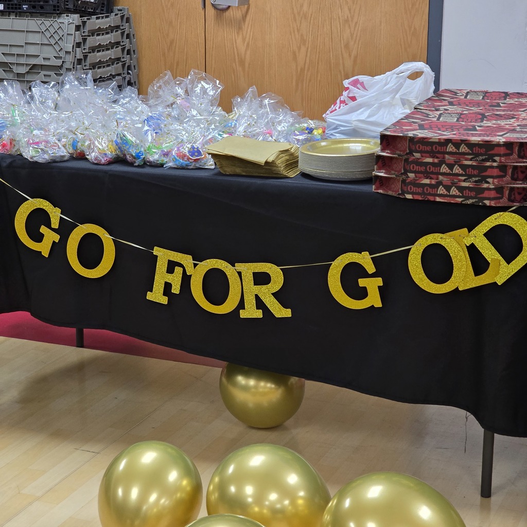 Table with balloons and a banner reading "GO FOR GOLD". Behind it, storage boxes, plastic bags, and a pizza box.