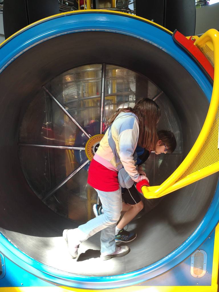 Two people, one in front of another, climbing up a yellow slide into a large blue tunnel.