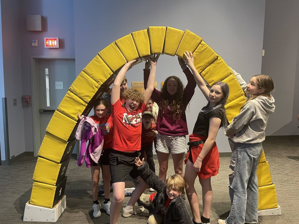 A group of young people are posing together. Some are holding onto a yellow arch.