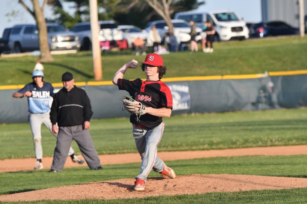 A baseball pitcher in a red hat winds up to throw the ball at a baseball game.