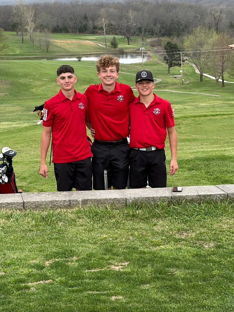 Three young men in red shirts and black pants pose at a golf course with a pond and trees.