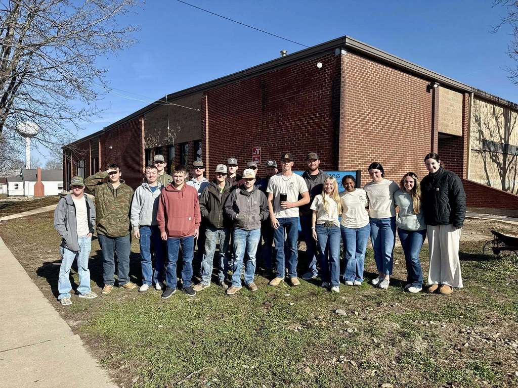 A group of individuals stands in front of a building with brick walls, posing for a photo.