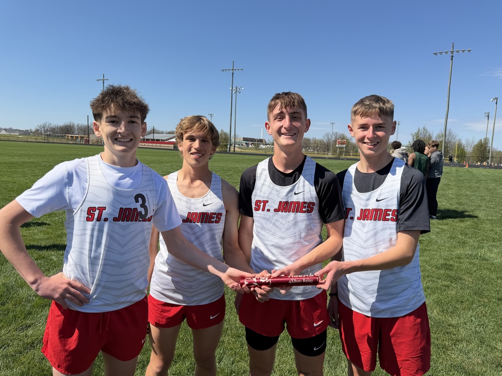 Four boys in matching uniforms pose for a photo on a grassy field. They hold a trophy.
