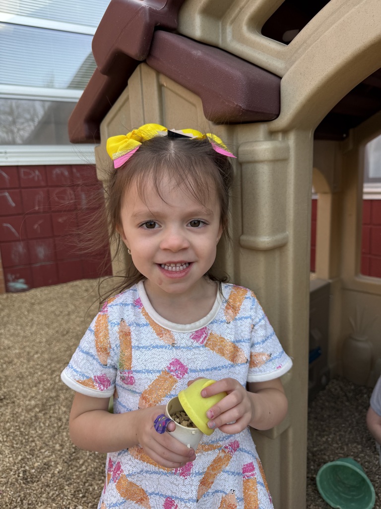 Young girl in a white dress with orange and pink designs holds a yellow container with yellow lid.
