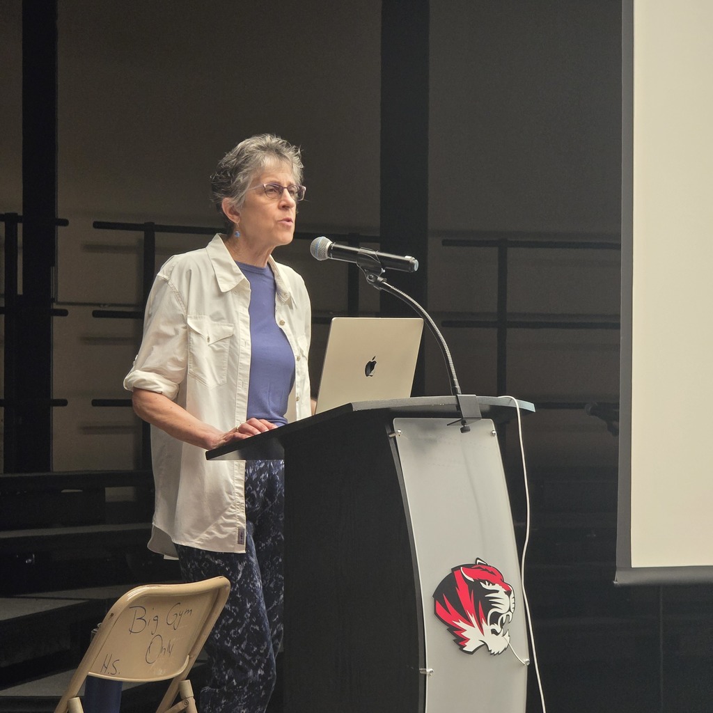 A woman speaks at a podium, with a laptop on it, in an auditorium.